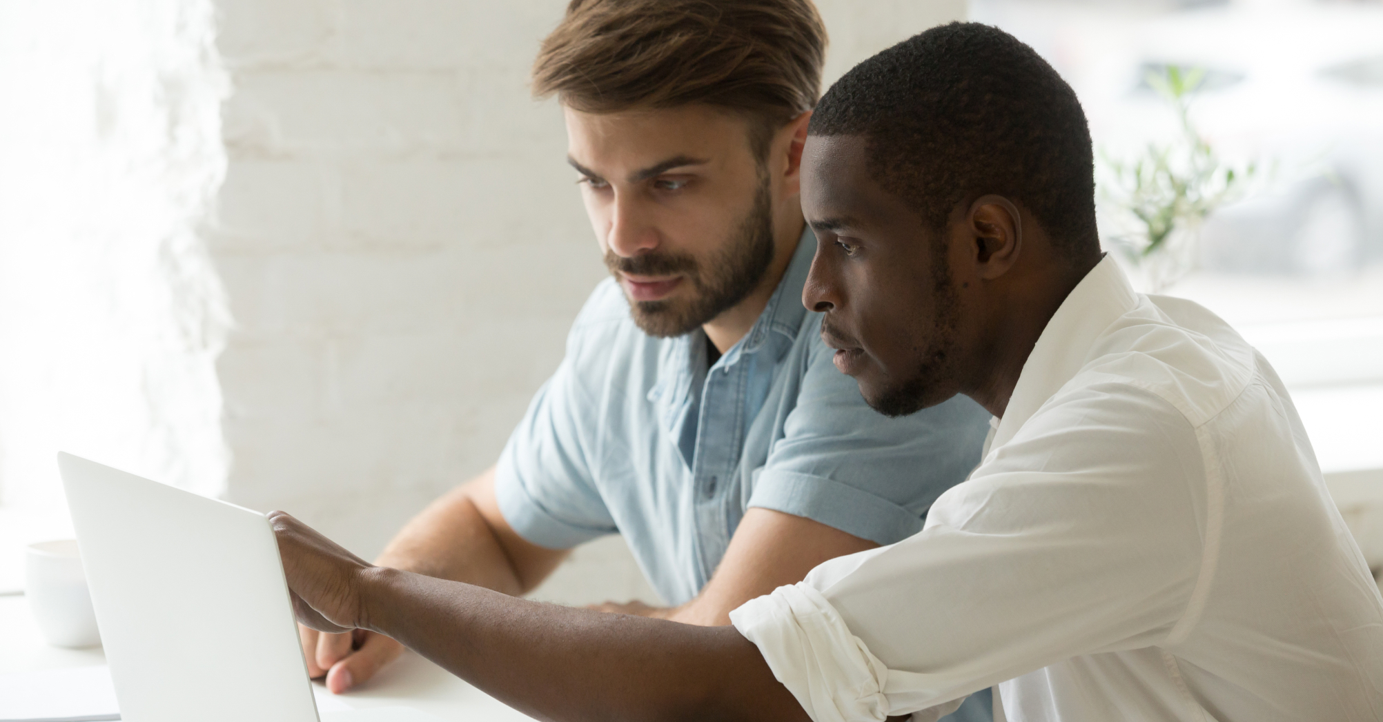 Two men are sitting in front of a laptop and collaborating on a project.